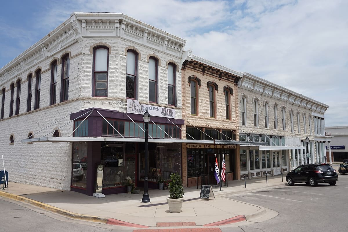 Two-story late 1800s limestone commercial buildings on Dallas Avenue in downtown Weatherford, with arched upper windows, bracketed cornices, and shop awnings over the sidewalk