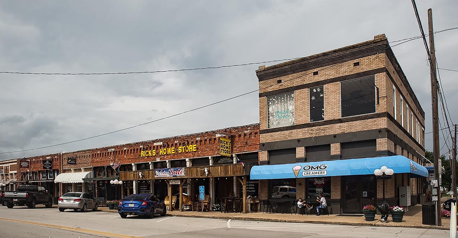 Brick storefronts on Ballard Avenue in historic downtown Wylie, Texas, led by a two-story tan brick building with a blue awning on the corner